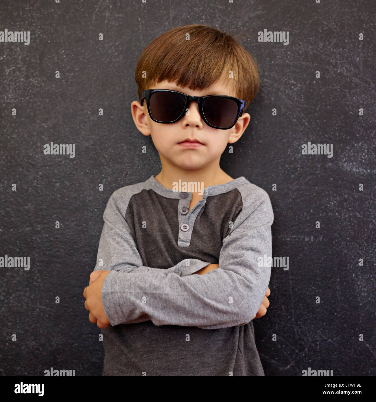 Portrait of little boy wearing sunglasses looking at camera with his arms  crossed. Small kid in front of a blackboard posing for Stock Photo - Alamy