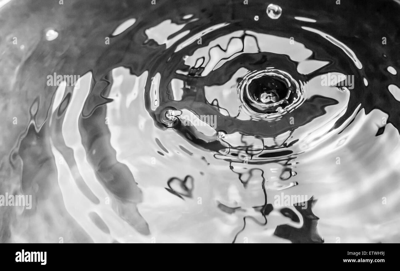 Water drops from a leaking pipe causing ripples on water surface in black and white Stock Photo