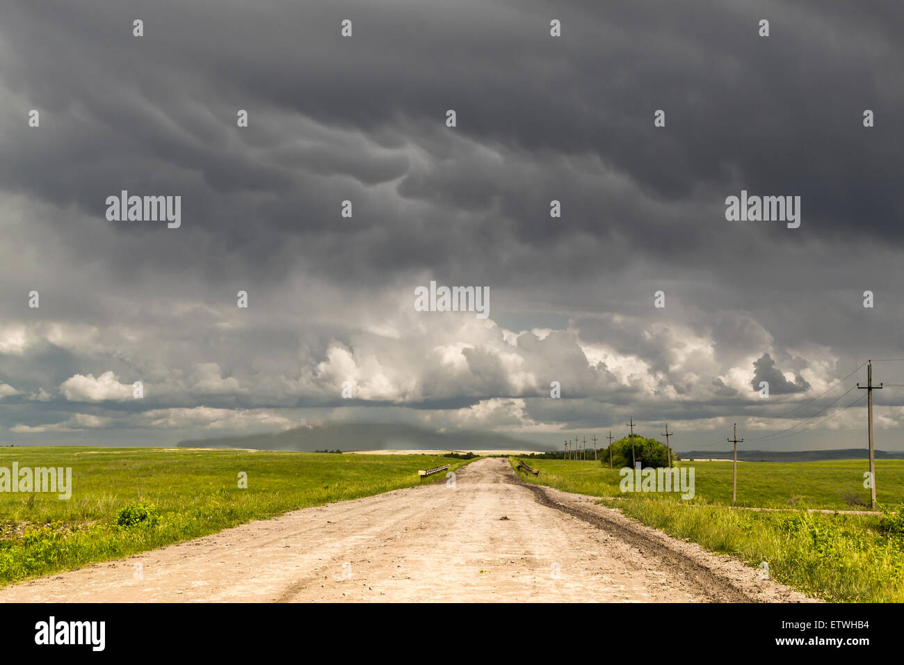Solitary dirt track leads to the horizon as dark rain clouds gather overhead Stock Photo