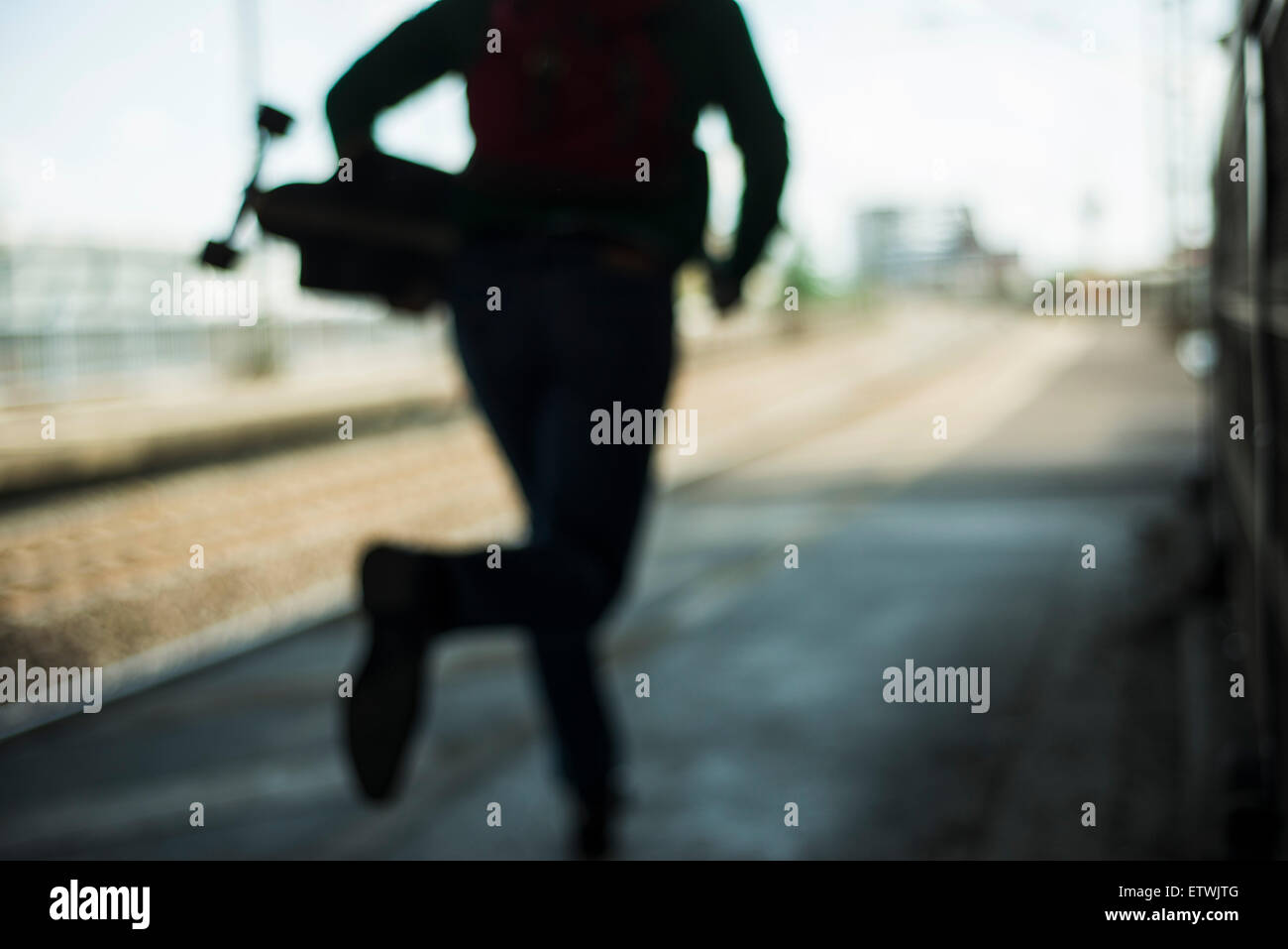 Blurred view of man with skateboard running on railway platform Stock Photo