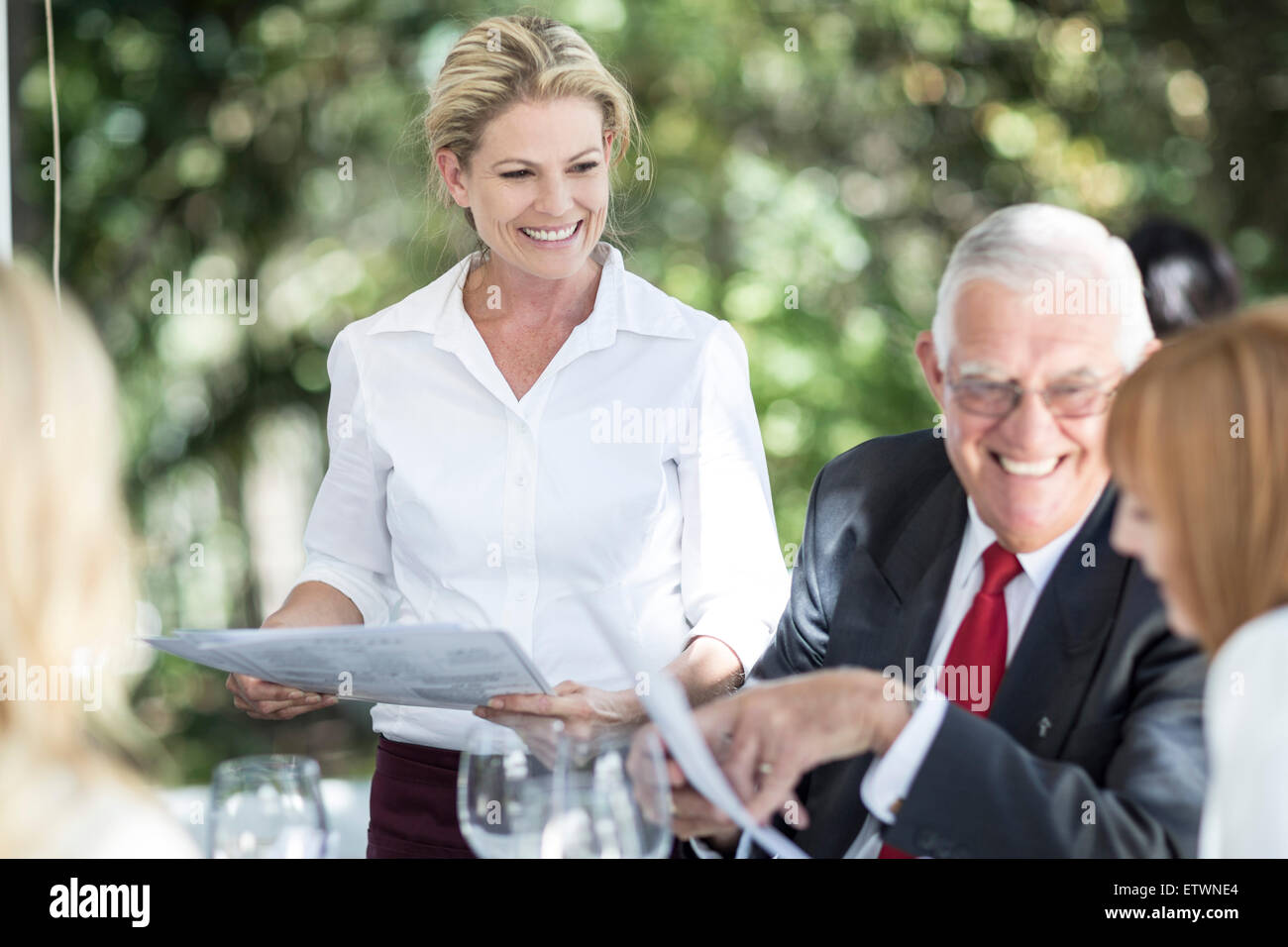 Waitress explaining menu to clients at table Stock Photo - Alamy