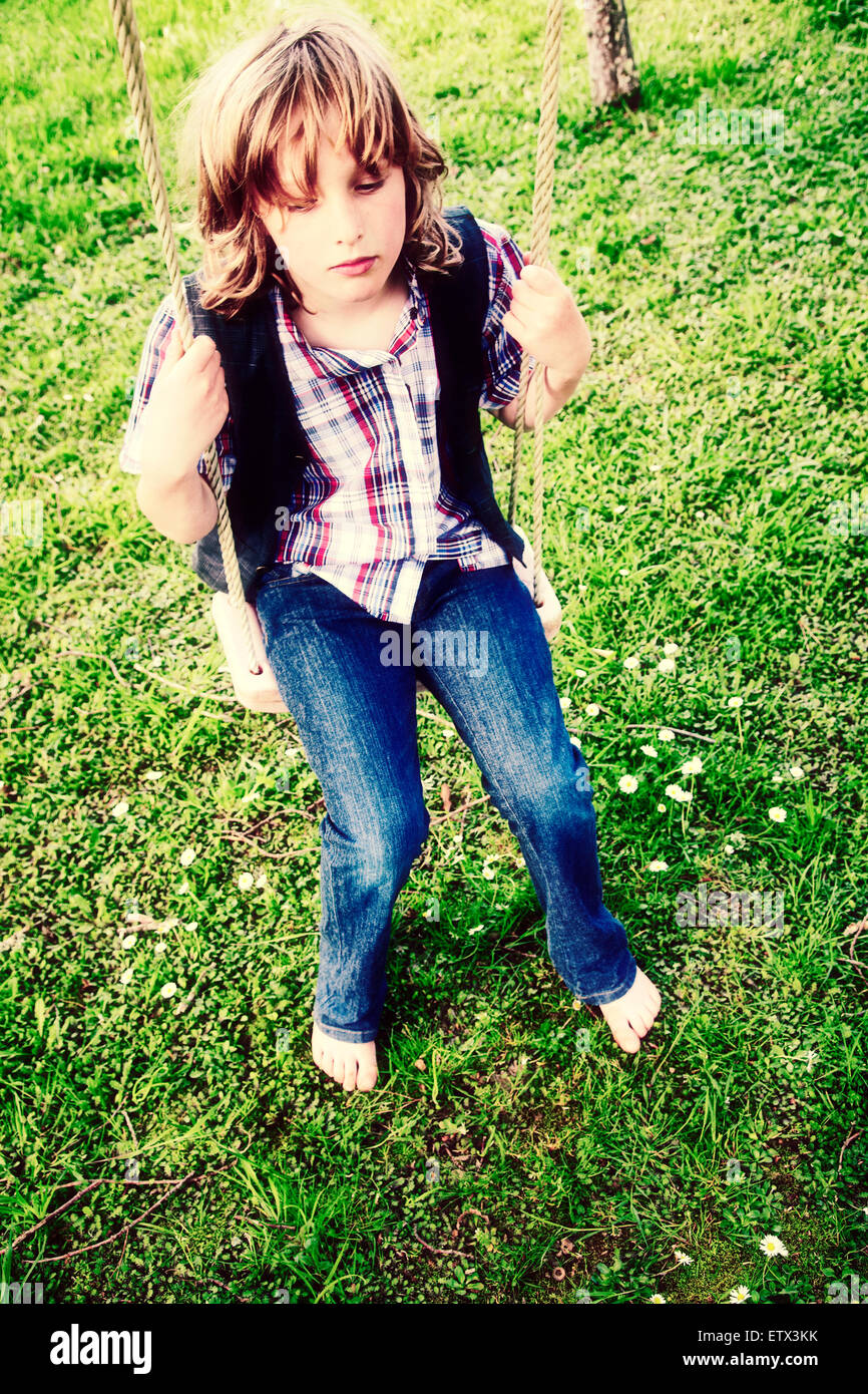 Blond haired boy aged 7 -10 years sitting on a swing Stock Photo