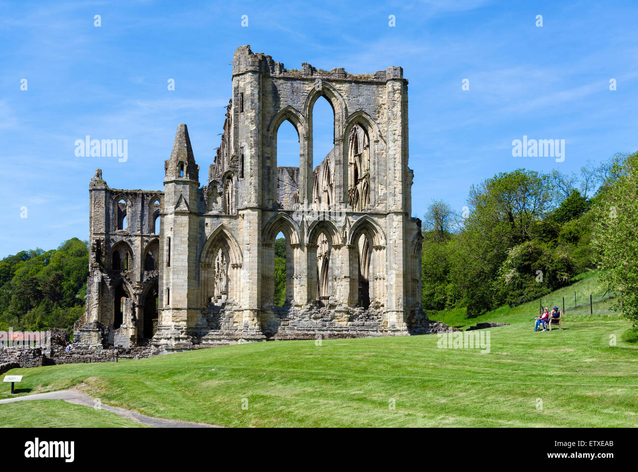 Couple sitting on a bench by the ruins of Rievaulx Abbey, near Helmsley, North Yorkshire, England, UK Stock Photo