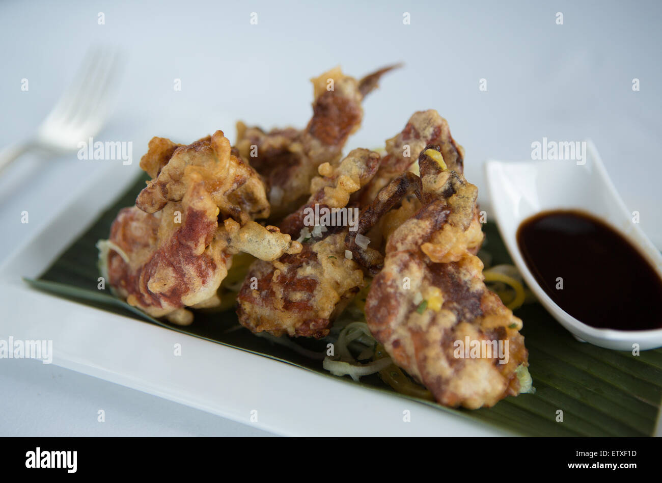 Soft shell crab on a bed of mango, cucumber salad and soy sauce dip served on a white plate