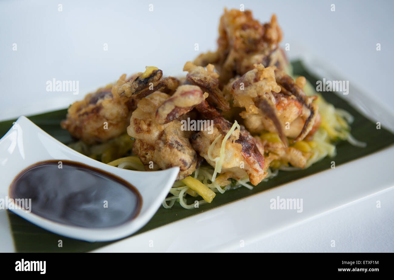 Soft shell crab on a bed of mango, cucumber salad and soy sauce dip served on a white plate