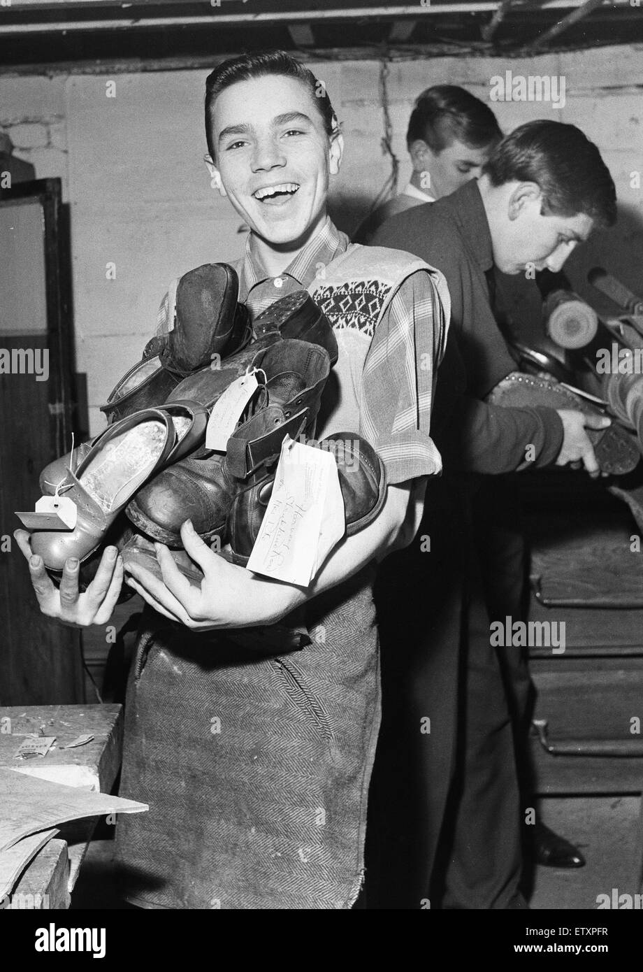 A boy carries a bundle of shoes. He is 'at work' at the Lion Boys Club in Hoxton, London, where members do shoe repairs for old age pensioners free of charge. The idea is to encourage the boys to help others. Leather for the repairs is bought with club fu Stock Photo