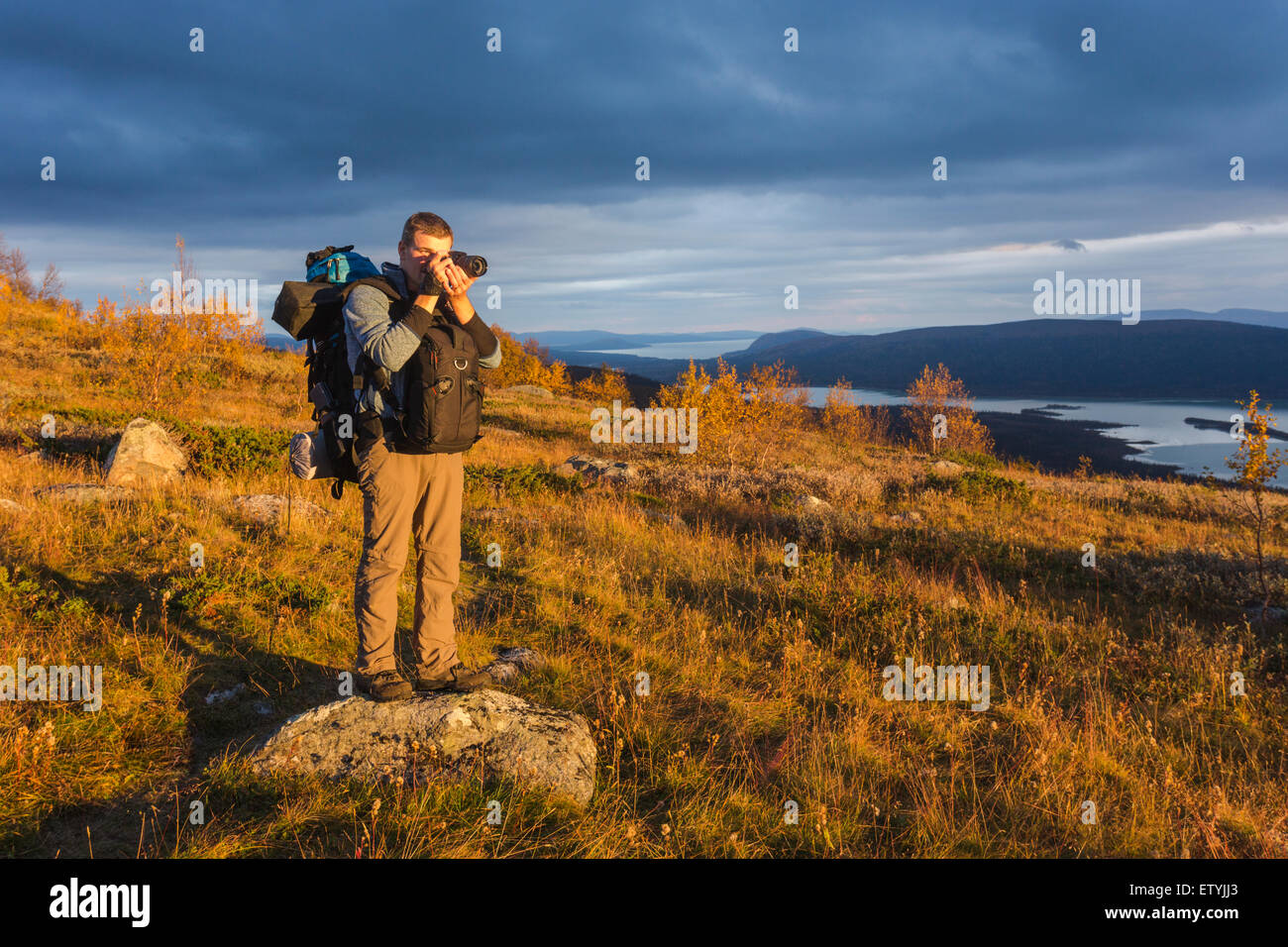 White man with backpack taking photo standing on mountain in autumn season in Sweden, Swedish lapland Stock Photo
