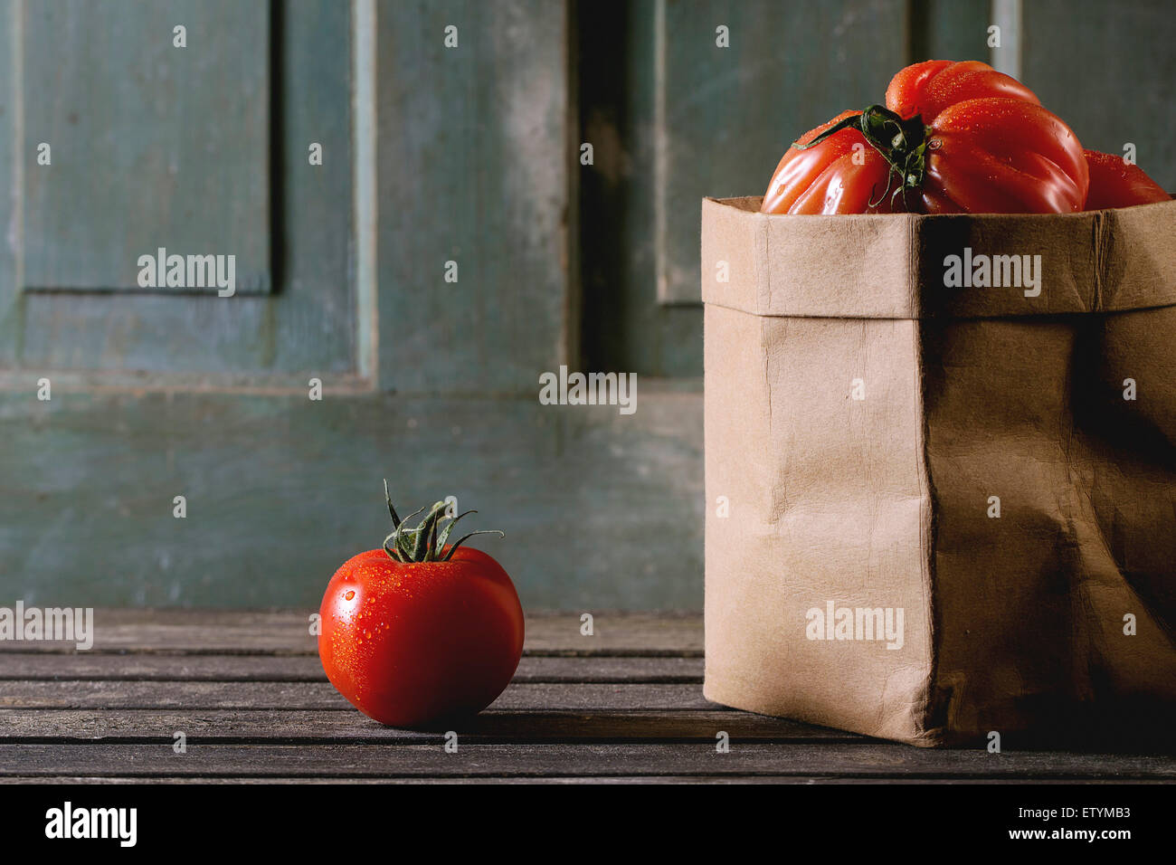 One and heap of big red tomatoes RAF in paper bag over old wooden table ...