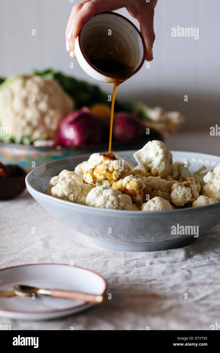 Raw cauliflower florets are being drizzled with a spicy dressing by a