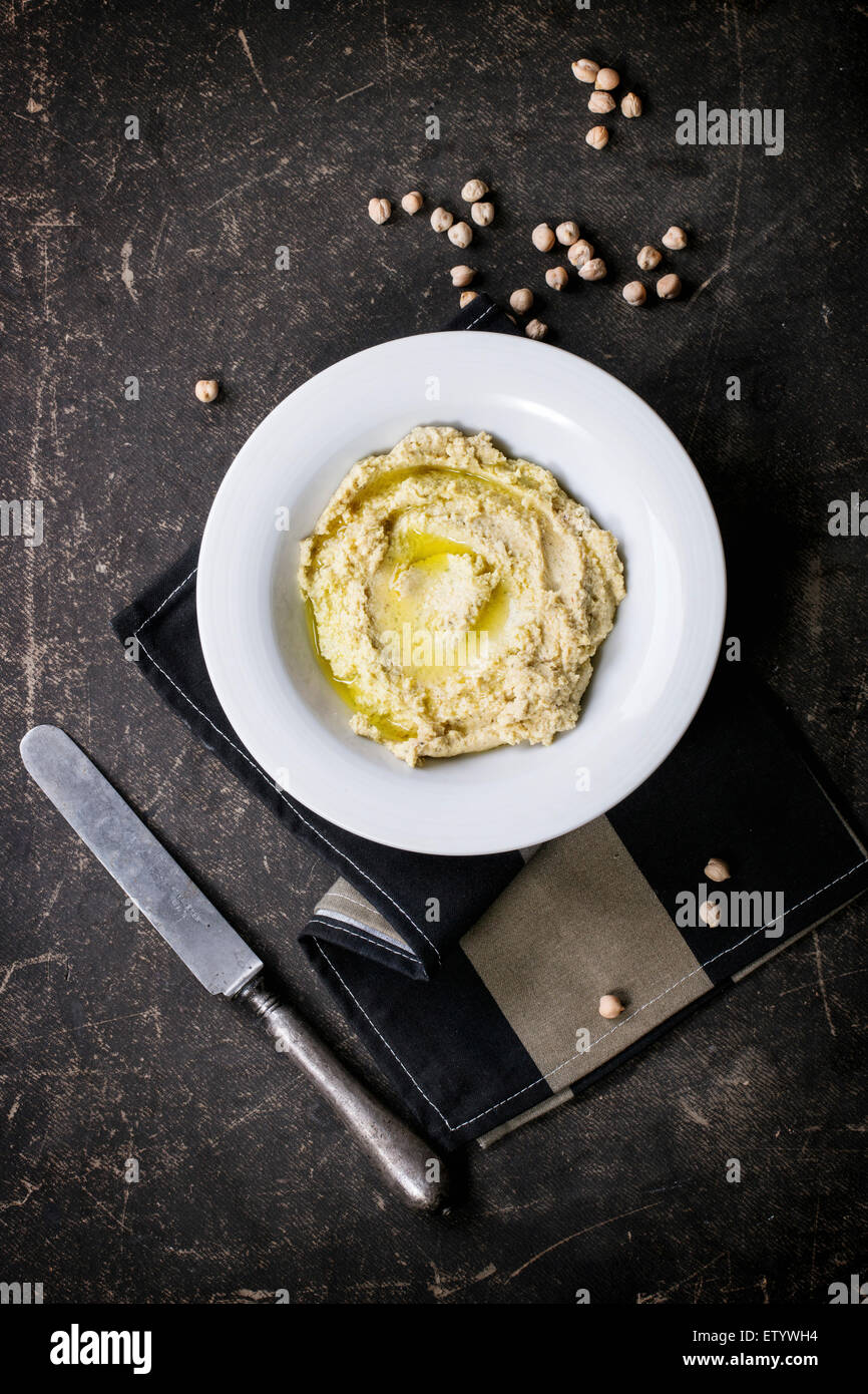 Plate of homemade hummus with vintage knife and raw chick-pea over dark table. Top view Stock Photo