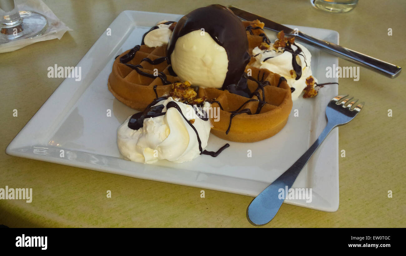 One big waffle with a big ball of vanilla flavored ice cream and chocolate, on a nice square shaped white plate. Stock Photo
