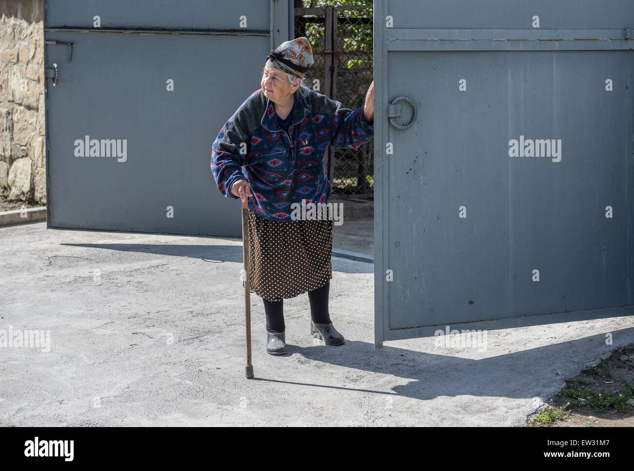 Old woman opening gate in UNESCO historical town of Mtskheta, Georgia Stock Photo