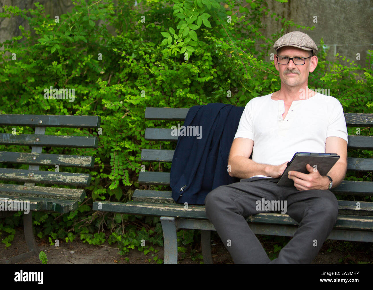 man sitting on a bench in a park with tablet in his hand Stock Photo