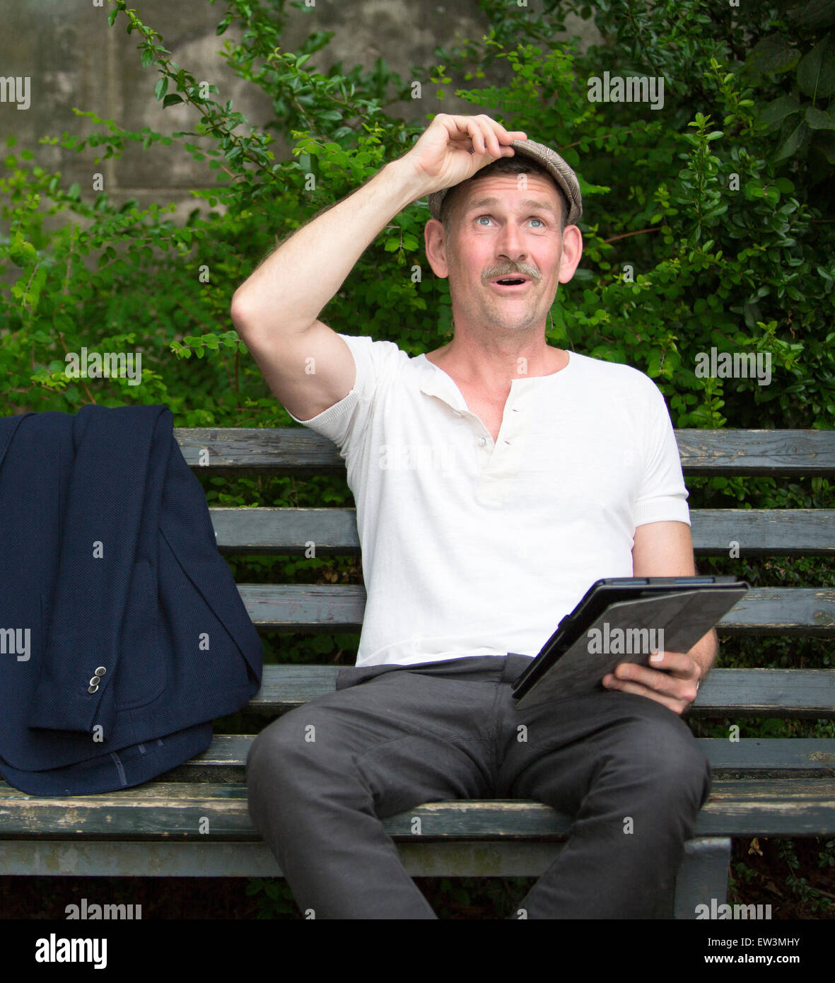 man sitting on a bench in a park with tablet in his hand Stock Photo