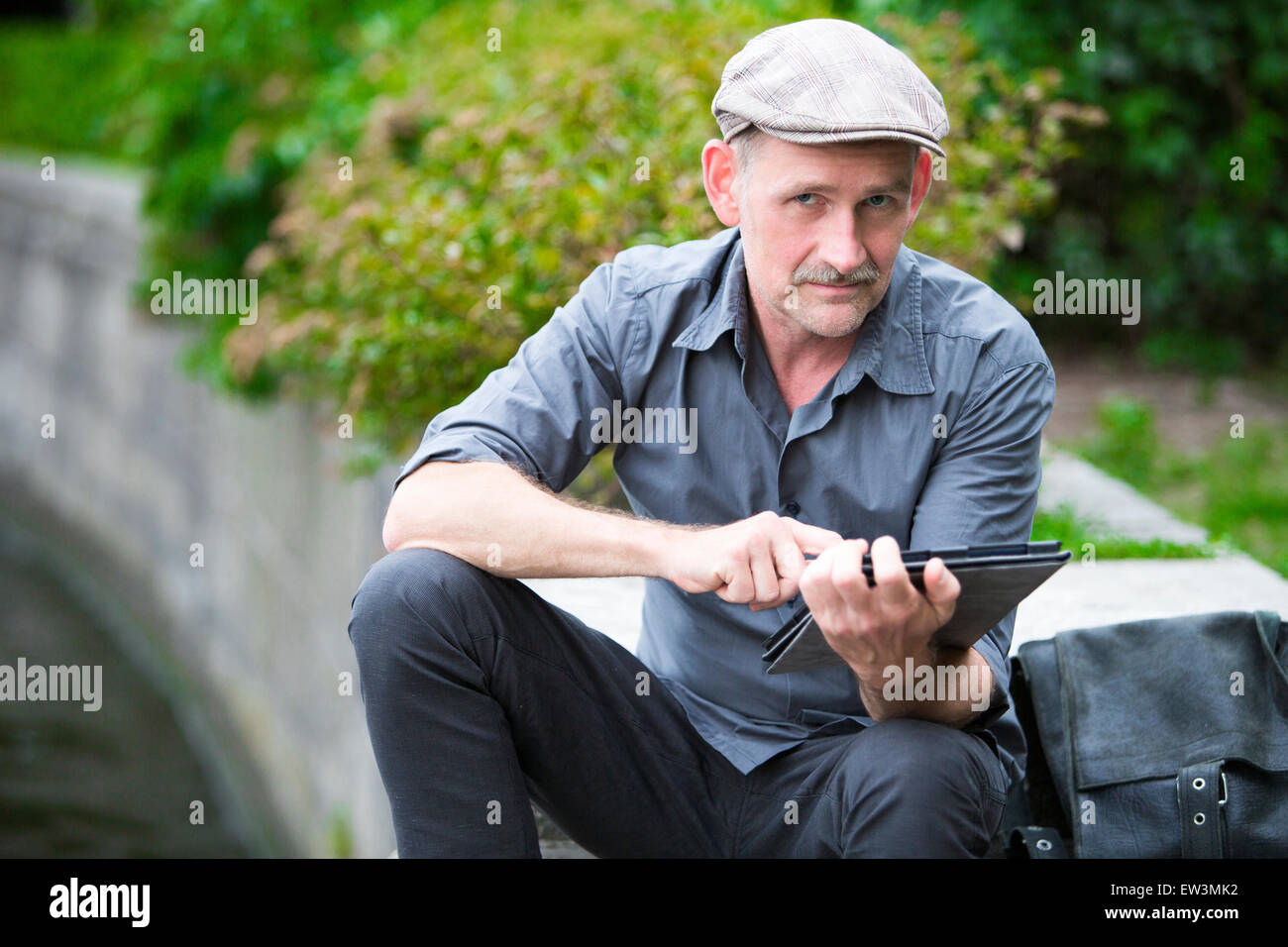 man sitting by the water with tablet in his hand Stock Photo