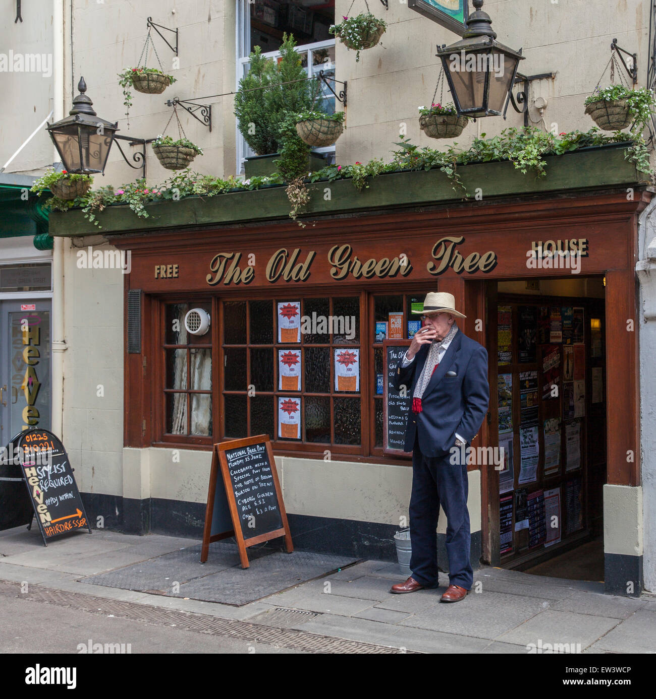 Man wearing a suit and a hat smoking a cigarette outside The Old Green Tree pub in the centre of Bath. Stock Photo