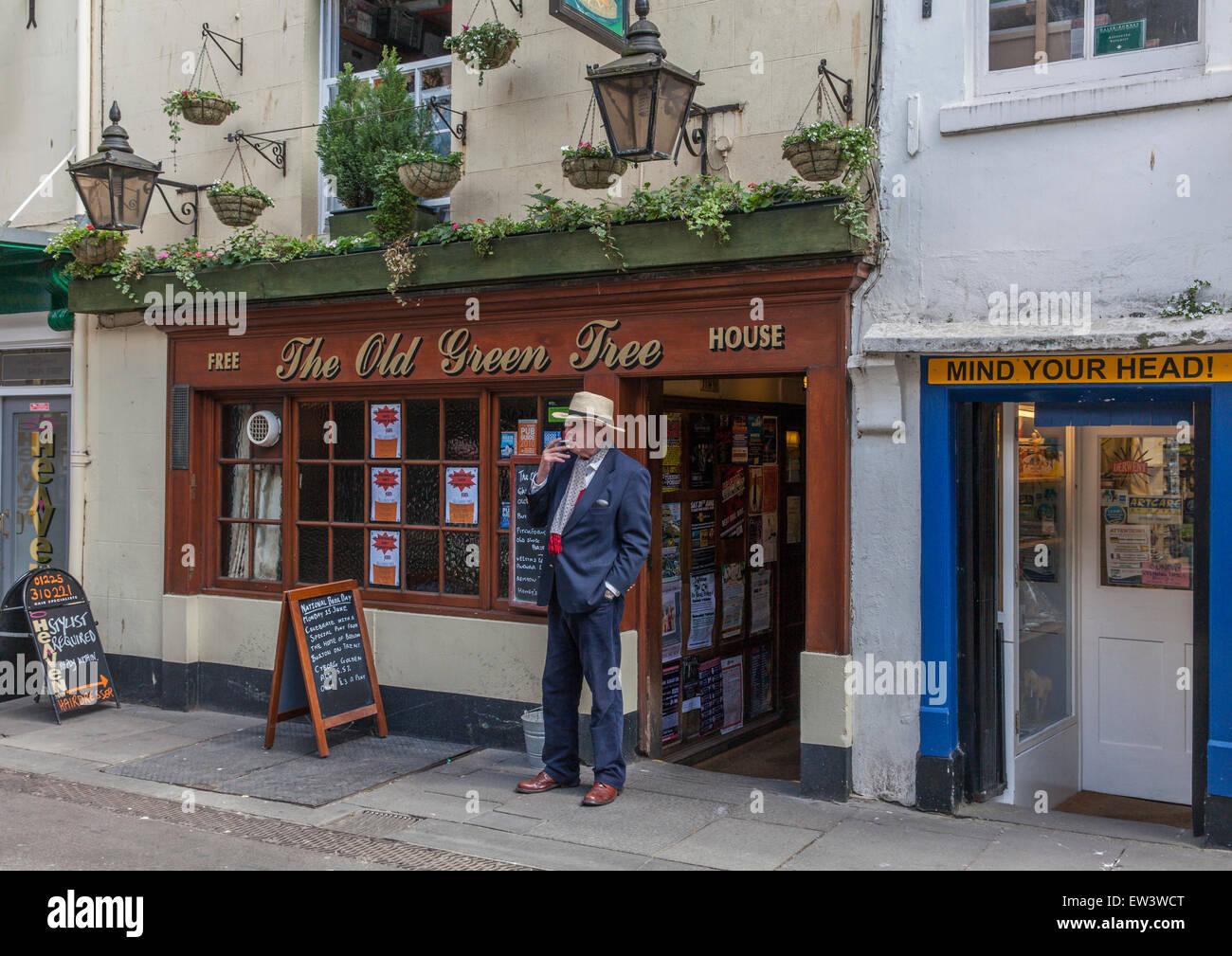 Well dressed gentleman in a suit with a hat smoking a cigarette outside The Old Green Tree pub in the centre of Bath. Stock Photo