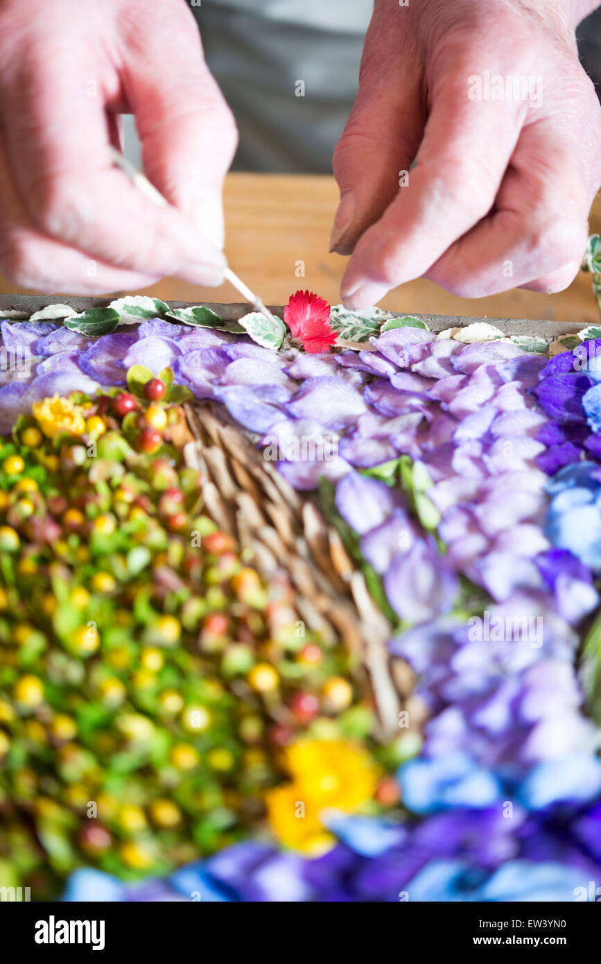 Holywell, UK. 17th June, 2015. Margaret Perryman decorates a wooden frame with thousands of individual flower petals and seeds to form an intricate mosaic picture that is displayed by the ancient well at the Church of St John the Baptist in the riverside village of Holywell, Cambridgeshire UK. The painstaking task is carried out by a team of local volunteers and starts with the design being pricked out in the clay, followed by the placing of individual petals pressed into the clay with a cocktail stick. Credit:  Julian Eales/Alamy Live News Stock Photo