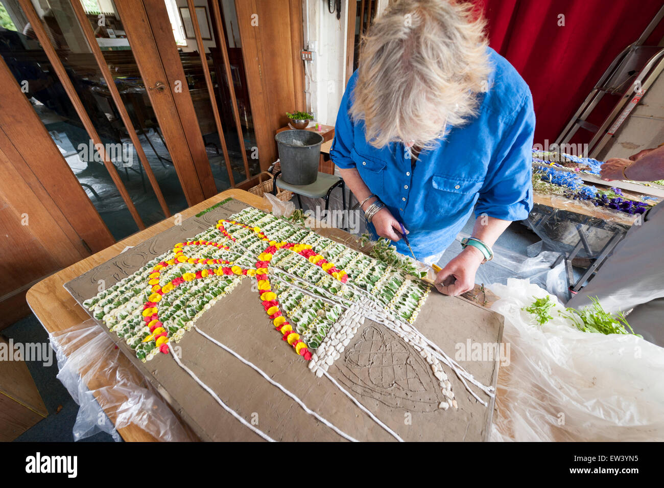 Holywell, UK. 17th June, 2015. Jill Harvey decorates a wooden frame with thousands of individual flower petals and seeds to form an intricate mosaic picture that is displayed by the ancient well at the Church of St John the Baptist in the riverside village of Holywell, Cambridgeshire UK. The painstaking task is carried out by a team of local volunteers and starts with the design being pricked out in the clay, followed by the placing of individual petals pressed into the clay with a cocktail stick. Credit:  Julian Eales/Alamy Live News Stock Photo