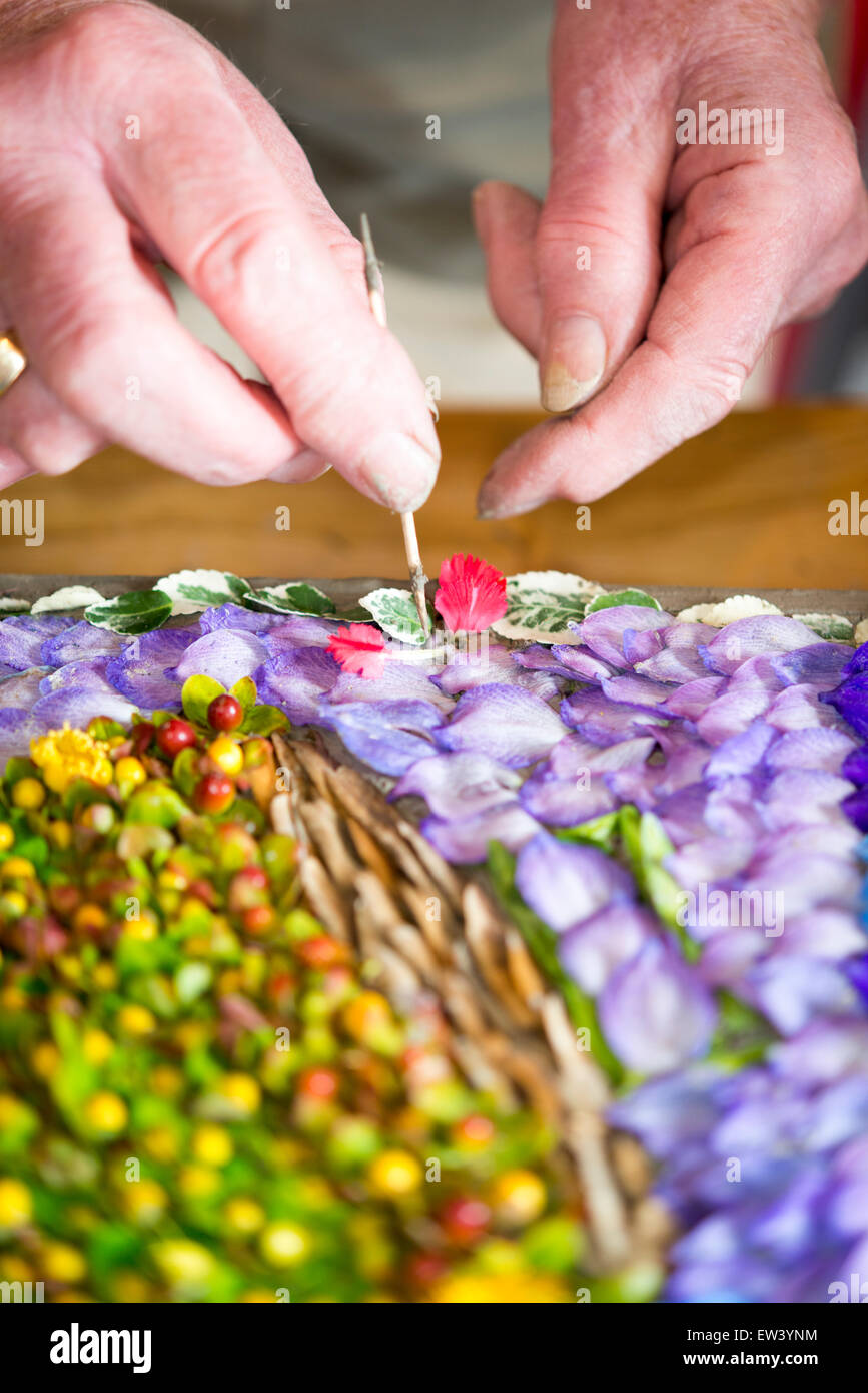 Holywell, UK. 17th June, 2015. Nadine Scott decorates a wooden frame with thousands of individual flower petals and seeds to form an intricate mosaic picture that is displayed by the ancient well at the Church of St John the Baptist in the riverside village of Holywell, Cambridgeshire UK. The painstaking task is carried out by a team of local volunteers and starts with the design being pricked out in the clay, followed by the placing of individual petals pressed into the clay with a cocktail stick. Credit:  Julian Eales/Alamy Live News Stock Photo