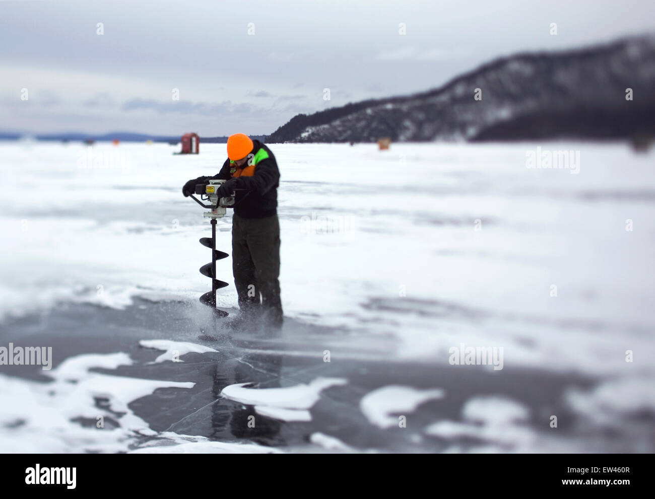An ice fisherman uses a skimmer to clear a just-opened hole on a