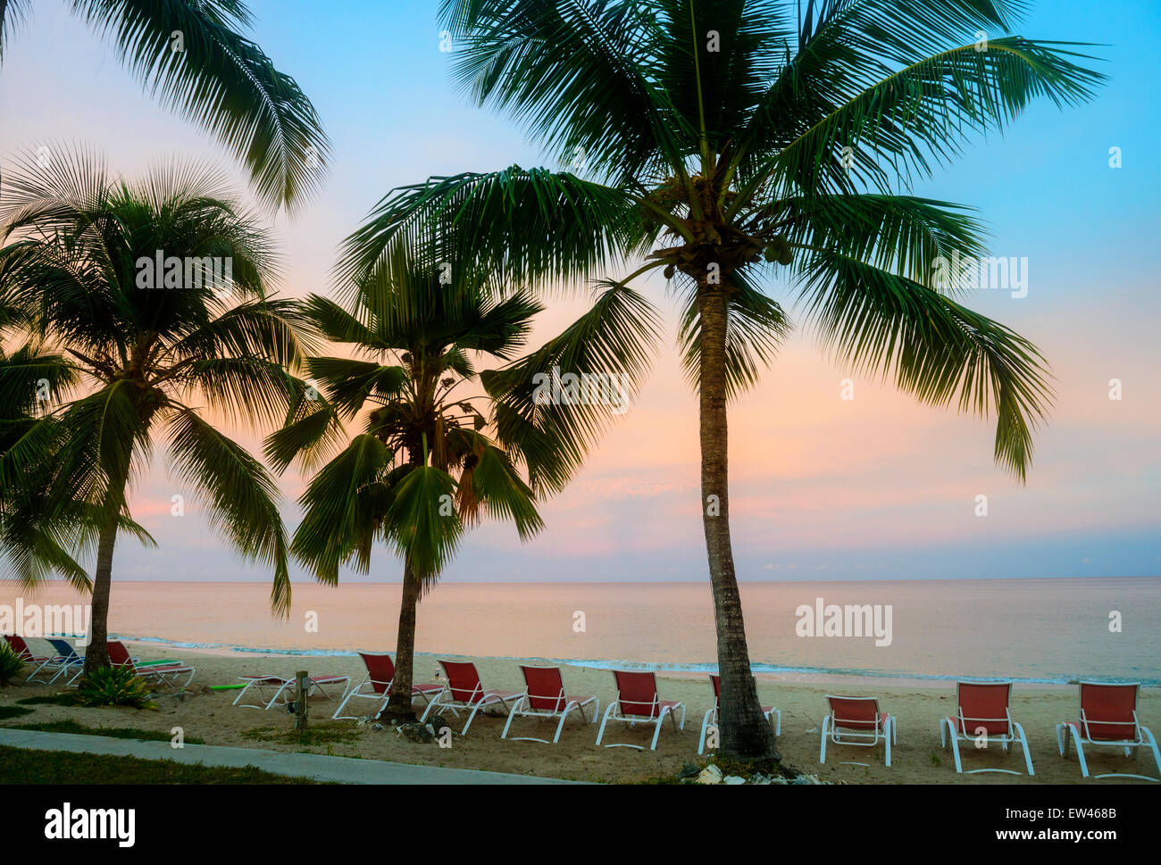 Sunrise paints delicate colors over the Caribbean on the isle of St. Croix, U.S. Virgin Islands. Beach, palms, beach chairs. Stock Photo