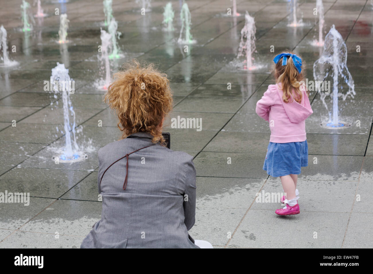 Woman taking photo of young girl playing in water feature at Brewery Square, Dorchester South, Dorset in June Stock Photo