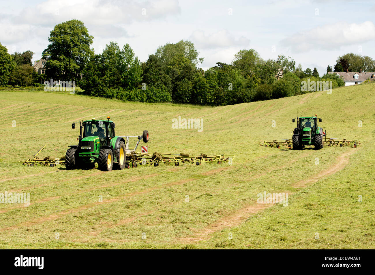 Two John Deere tractors turning hay, Northamptonshire, England, UK Stock Photo