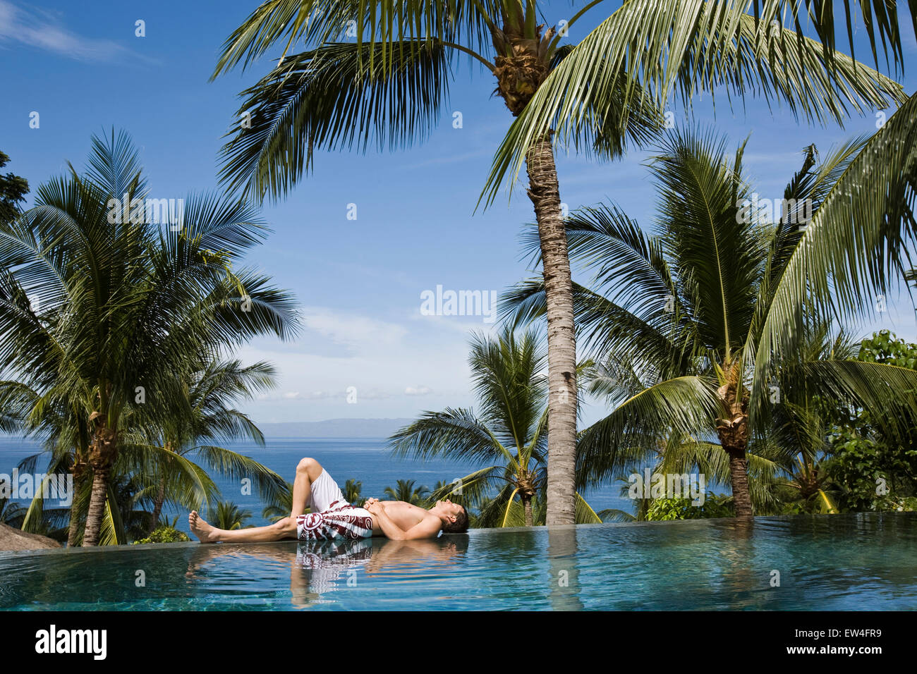 A man relaxing by the pool under a palm tree Stock Photo - Alamy