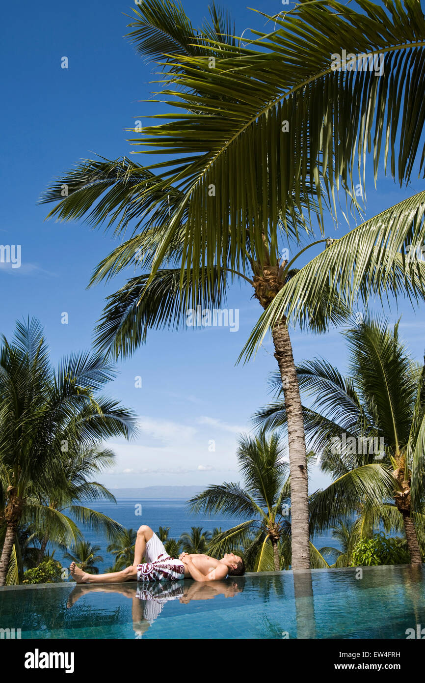 A man relaxing by the pool under a palm tree Stock Photo - Alamy