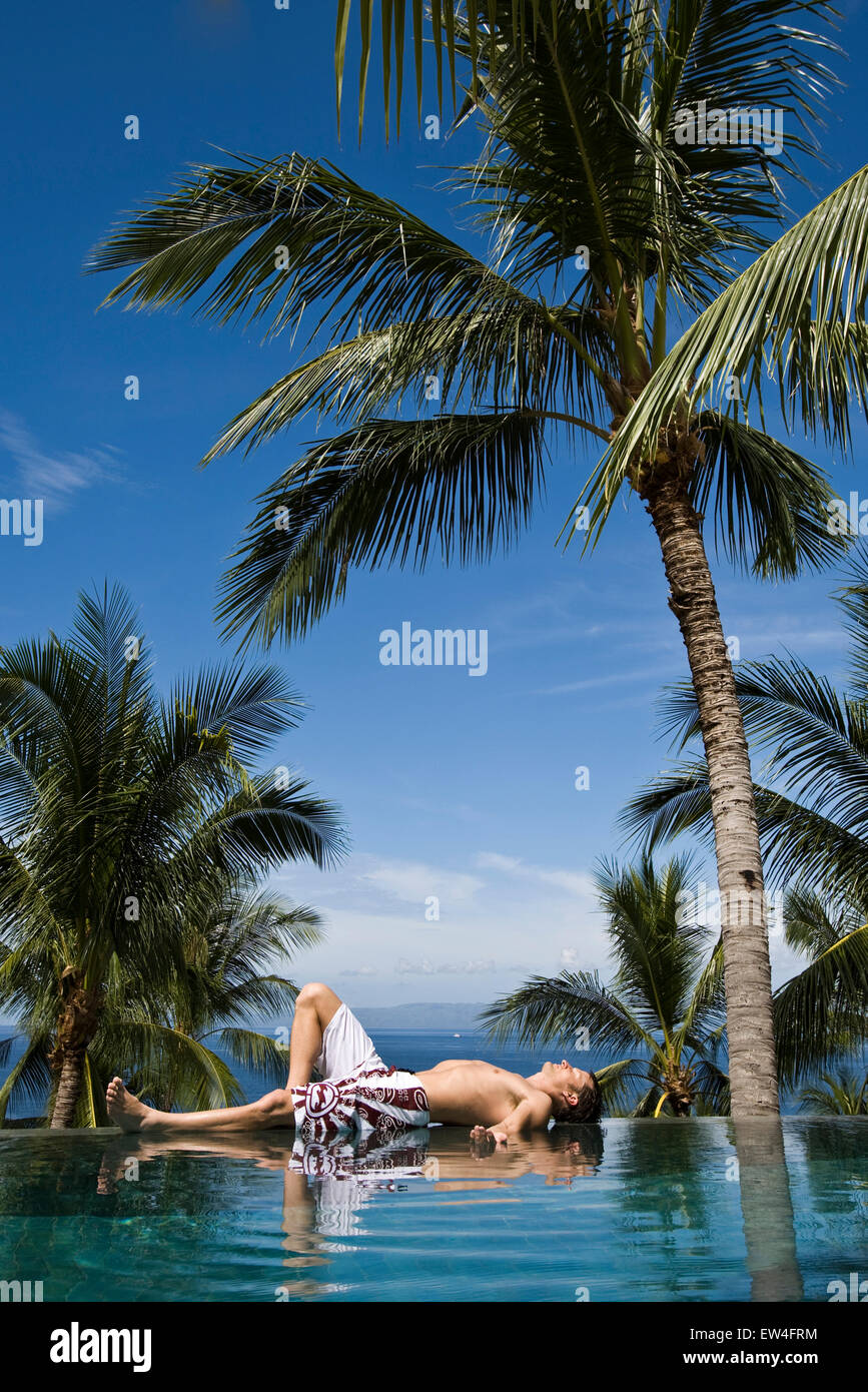 A man relaxing by the pool under a palm tree Stock Photo - Alamy