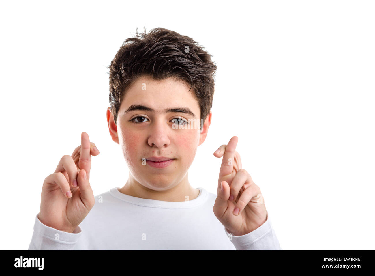 Latin young boy with acne in a white long sleeve t-shirt smiles crossing fingers of both hands as superstitious gesture to get luck Stock Photo