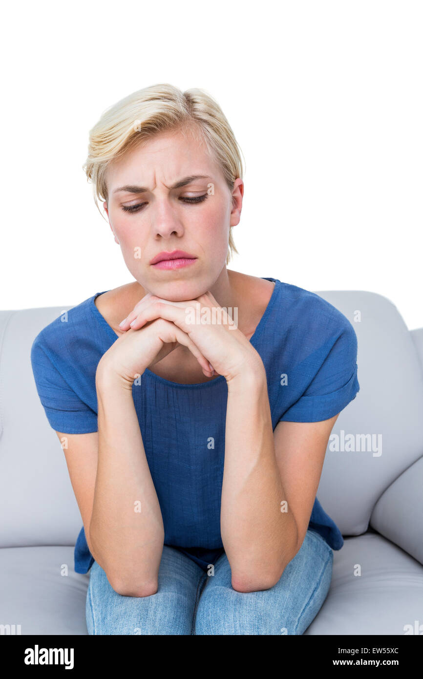 Thoughtful blonde woman sitting on the couch Stock Photo