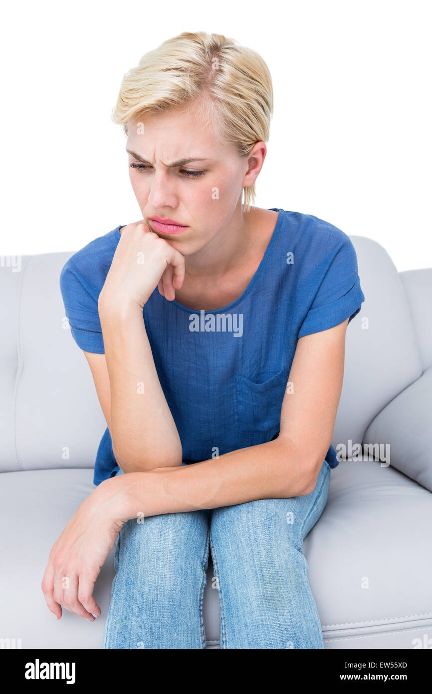 Thoughtful blonde woman sitting on the couch Stock Photo