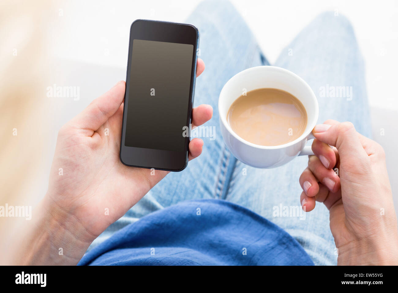 Woman using her mobile phone and holding cup of coffee Stock Photo