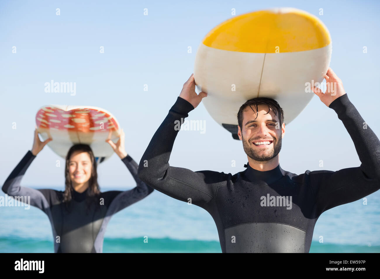 happy couple in wetsuits with surfboard on a sunny day Stock Photo