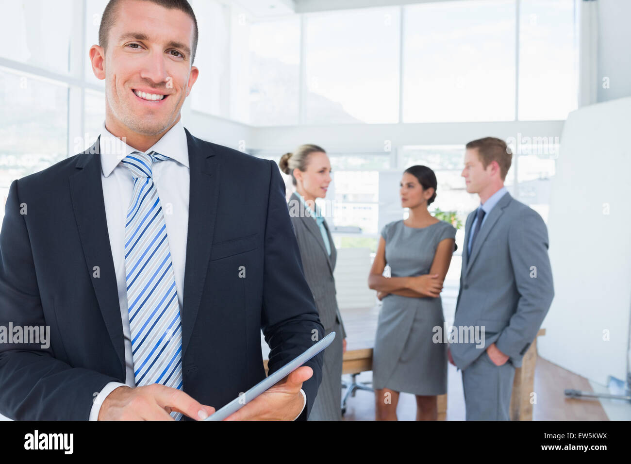 Businessman using tablet with colleagues behind him Stock Photo - Alamy