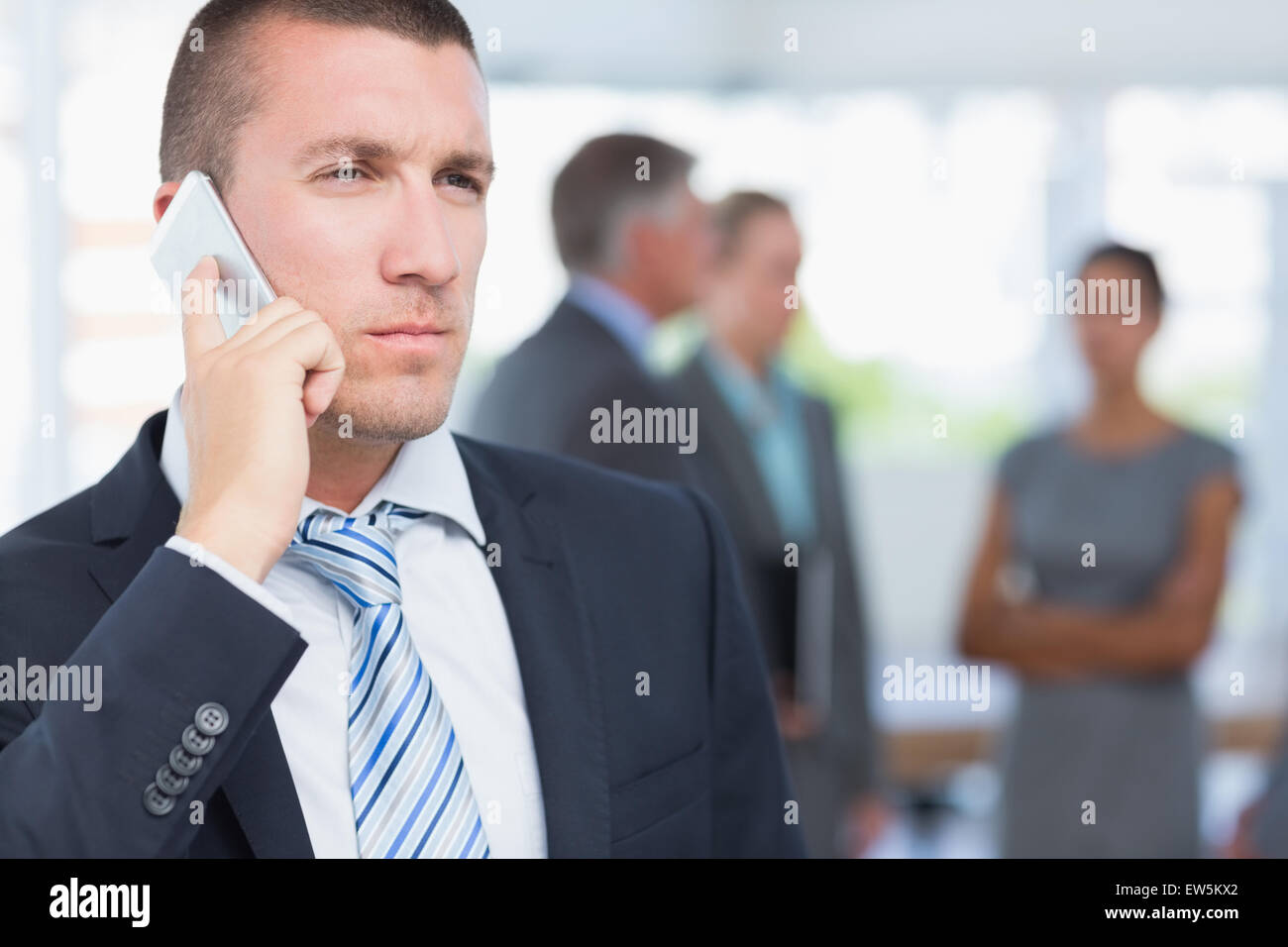 Businessman on the phone with colleagues behind him Stock Photo - Alamy