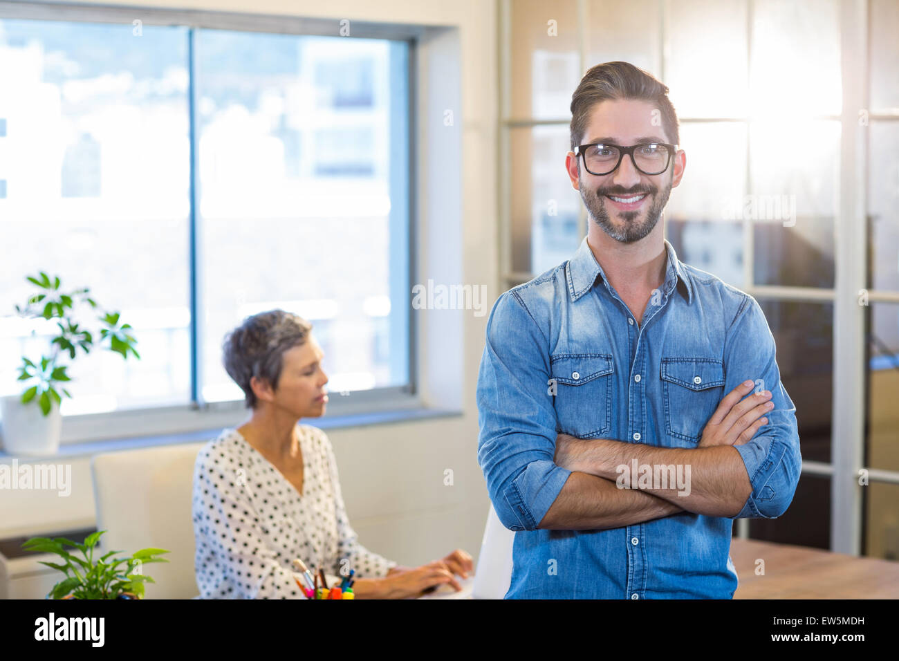 Smiling man standing arms crossed with his partner behind Stock Photo