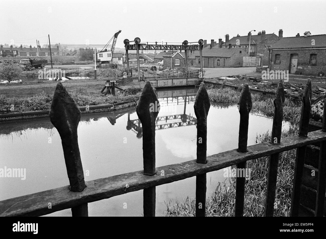Railings, blackened by 150 years of industrial smoke separate the weed grown banks of the Birmingham Wolverhampton Canal at Factory Locks, Tipton, from a railway coalyard. In the centre is an unusual mid 19th century lifting bridge over the U bend of the Stock Photo