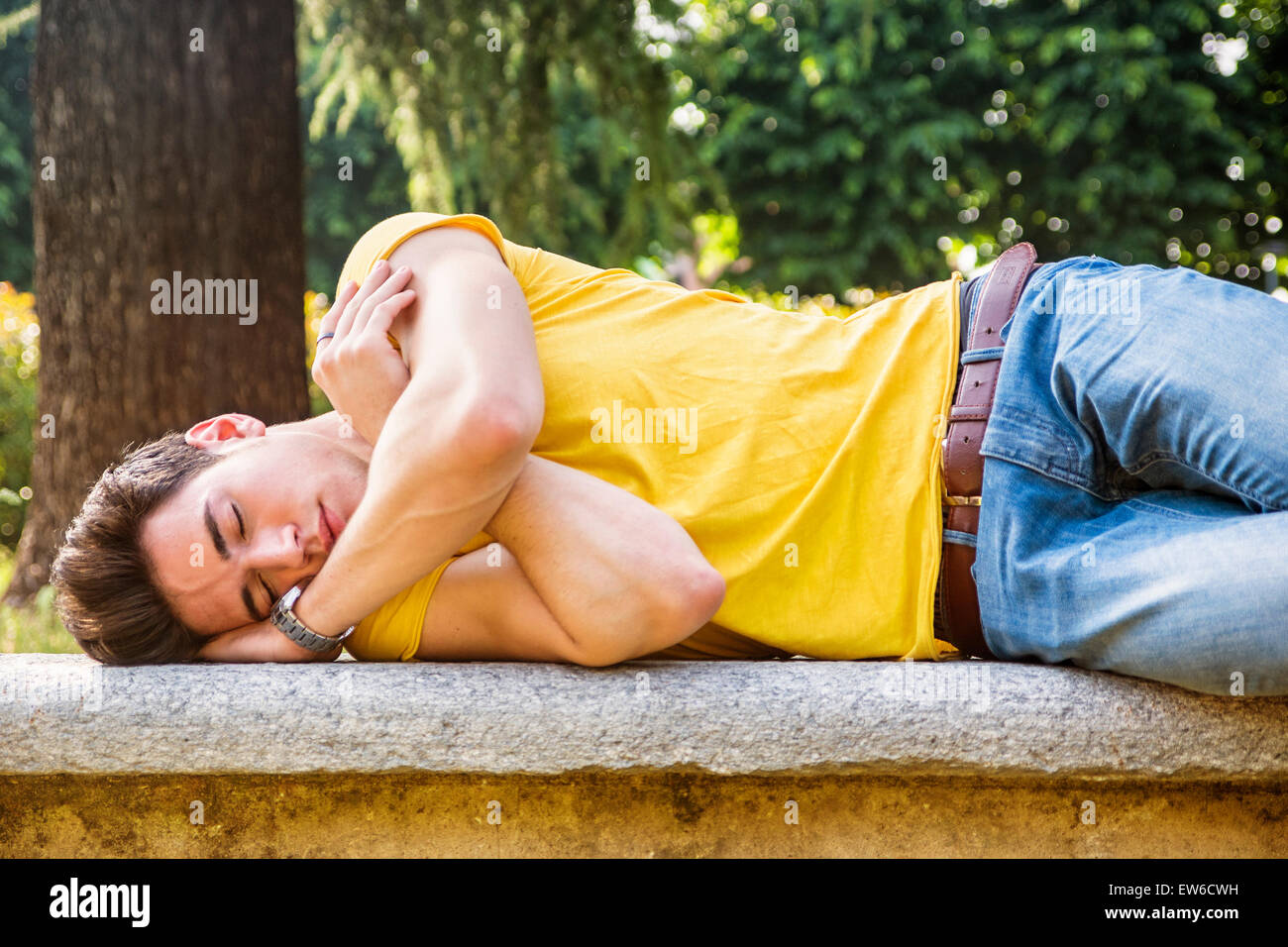 Attractive young man sleeping on stone bench outdoor in city park during day Stock Photo