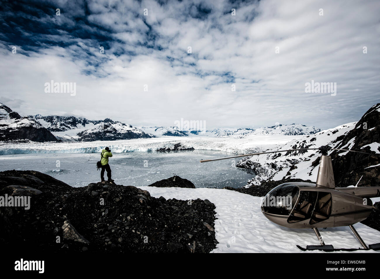 A man taking photos of a melting glacier with a helicopter waiting nearby.   Alaska, USA. Stock Photo