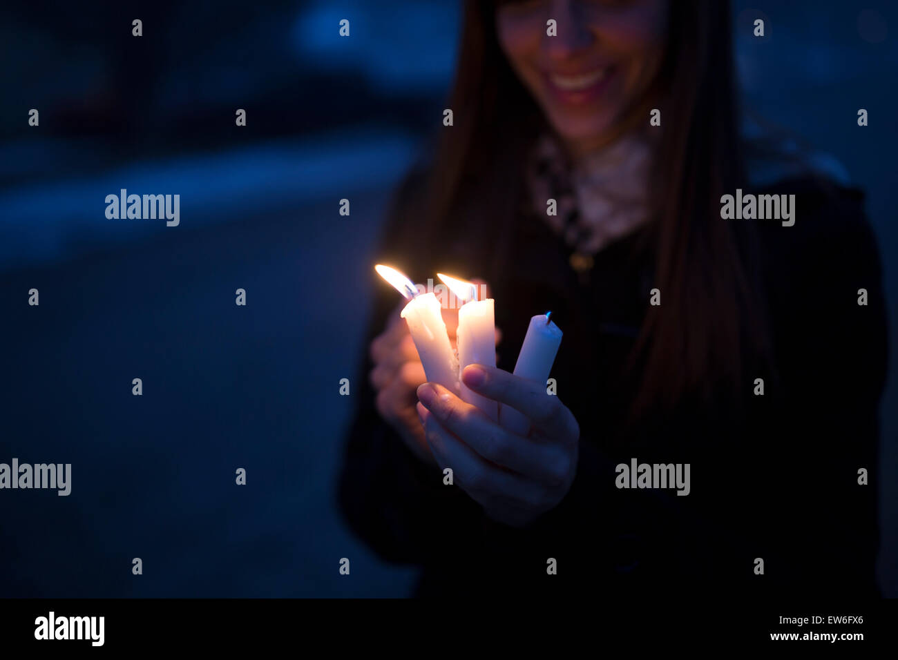 A young woman holds three candles in the twilight of a street. Stock Photo