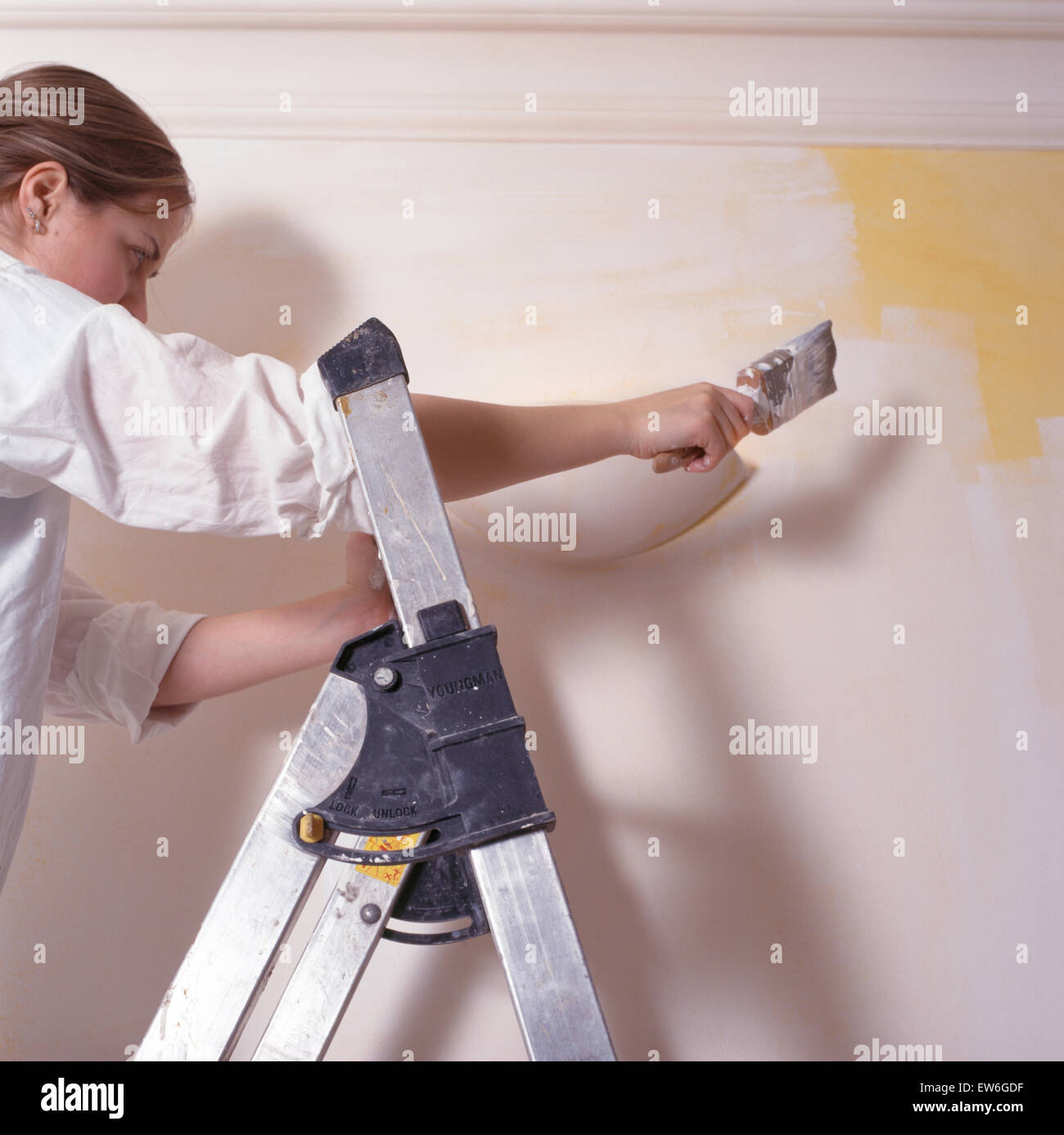 Woman on a step-ladder painting a room with white paint Stock Photo
