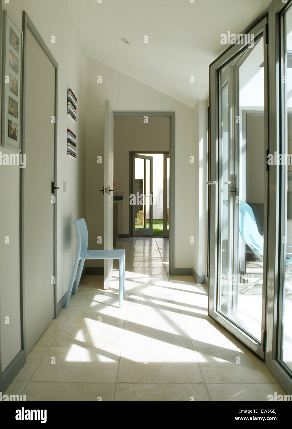 Glass bi-fold doors in modern hall with pale blue chair and limestone flooring Stock Photo