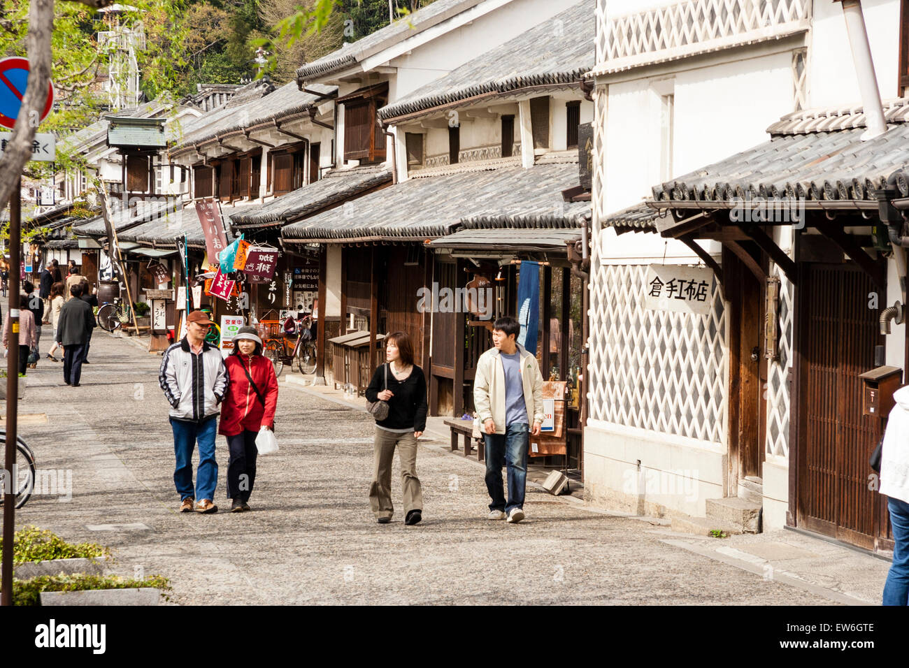 View along the waterfront avenue with tourists walking along past a row of traditional shops. Part of the Bikan historical area of Kurashiki, Japan. Stock Photo