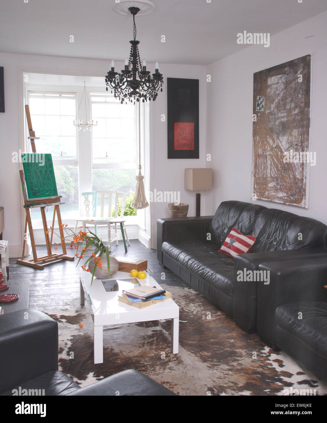 Black leather sofas and a white coffee table in artist's coastal living room with a vintage cow hide rug on floor Stock Photo