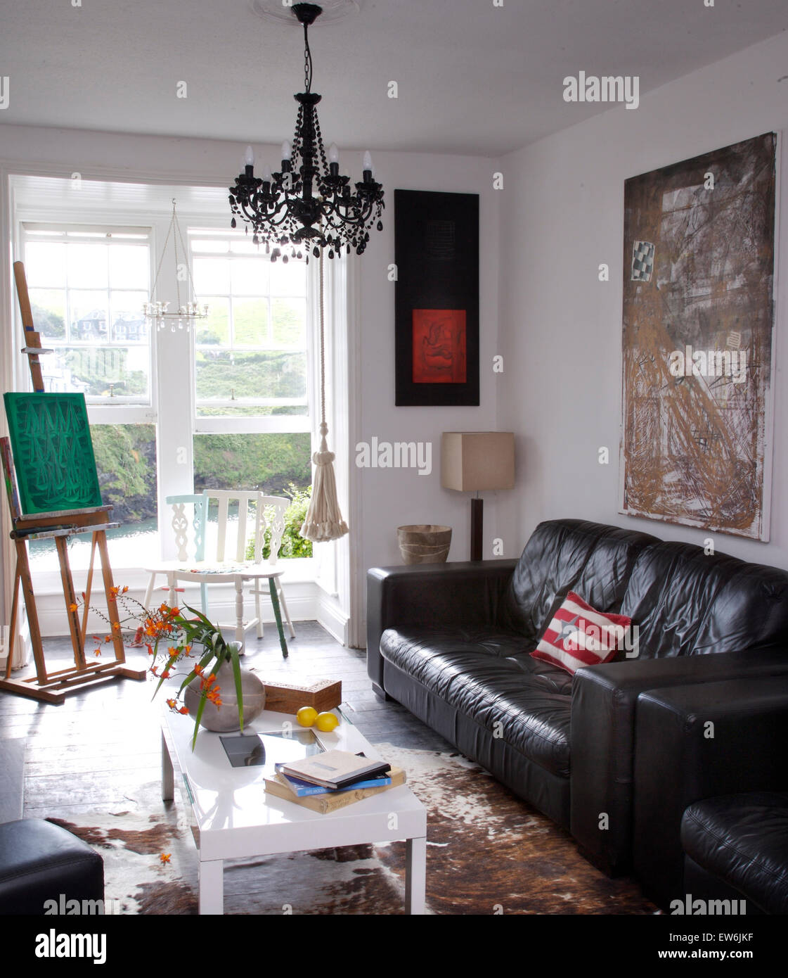 Black leather sofa in artist's coastal living room with an easel beside open windows with a view of the sea Stock Photo