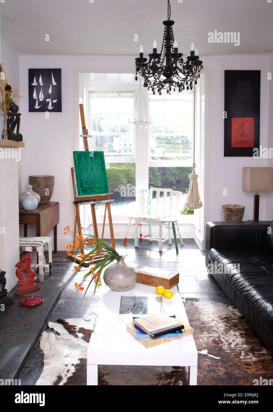 White coffee table in artist's coastal living room with an easel beside open windows with a view of a Cornish bay Stock Photo