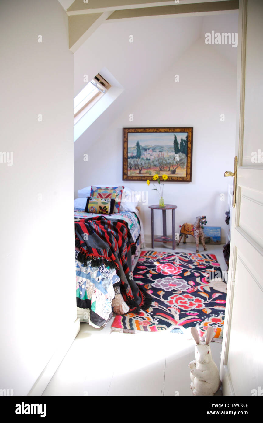 Door open to cottage bedroom with brightly coloured floral rug on floor beside bed Stock Photo